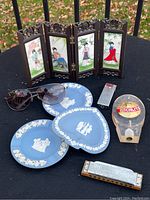 Photo showing all items including three Wedgwood ashtrays, geisha screen, Schmitz beer tap pull, Hohner harmonica, lighter, and sunglasses arranged on a black outdoor surface.