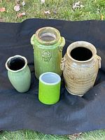 Four ceramic vases displayed on black cloth outdoors, showing two large handled vases, one tall narrow vase, and one small bright green vase.