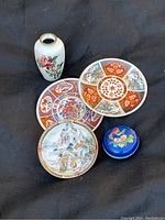Photo of lot including Japanese cloisonné vase, Chinese cloisonné box, and three Imari porcelain plates with various traditional designs.