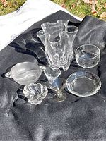 Overview of Finnish clear crystal vase with wavy edges and several accompanying cocktail glasses, bowls, and a plate displayed on black fabric outdoors.