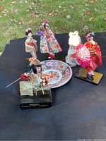 Overview of five Japanese dolls arranged around the Imari plate on a black cloth