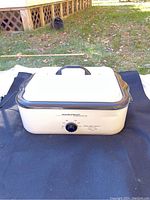 Front view of Hamilton Beach electric roaster oven resting on black cloth outdoors, showing temperature control knob and lid with handle.