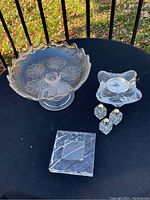 Photo showing all items on an outdoor table: footed glass compote dish, small glass candle holder with tealight, three small glass salt and pepper shakers, and square glass plate.
