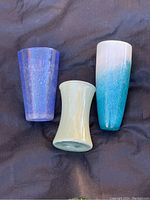 Three vases arranged upright on a dark fabric, showing blue, green and white-blue gradient colors.