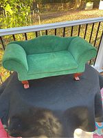 Front view of the green velvet mini couch showing curved armrests and seat cushion on black cloth outdoors.