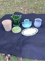 Front view of six mixed ceramic items including plant pots, vases, and plates arranged on a black cloth outdoors