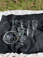 Seven various glass items including two vases, decorative glasses, bowl, cube container, arranged on fabric outdoors