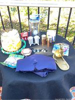 Full overview of assorted items on black tablecloth including brass kangaroo, glass container, blue heating pad, packages, and other small items