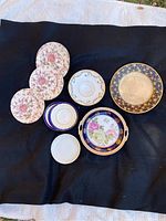 Top-down view of nine assorted vintage plates arranged on dark fabric outdoors to highlight floral designs and blue gold patterned rims.