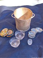 Metal ice bucket, floral patterned coasters, clear glass coasters, three ice cream bowls, small clear glass toothpick holder on dark fabric background