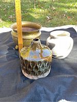 Brass planter and two ceramic vases on black cloth outdoors with ruler showing height
