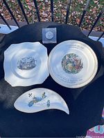 Three ceramic souvenir plates and a coin in lucite shown on black surface outdoors