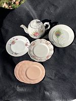 Front view showing teapot and six assorted dessert plates on black fabric