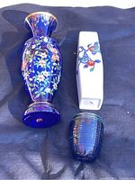 Photo showing all three vases placed on dark fabric background, including tall cobalt blue floral glass vase, rectangular ceramic vase with floral design, and small dark blue ribbed glass vase.