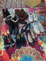 Photo showing 9 pairs of women's shoes including boots, sneakers, flats, heels, and sandals arranged on a colorful rug outdoors.