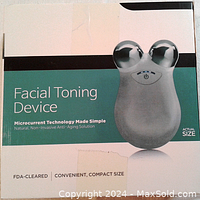 Front of packaging showing actual size image of the device with dual rounded metal massage heads, highlighting FDA-cleared, compact size, and microcurrent anti-aging technology.
