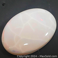 Close-up photo of the polished natural opal gemstone cabochon showing milky white color and faint internal veining with red flashes.