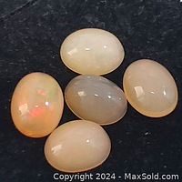Five natural genuine opal cabochon gemstones on a black background, highlighting their milky white translucence and fiery color flashes.