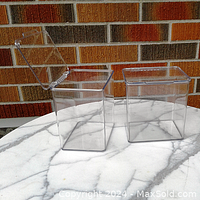 Two clear plastic stackable kitchen storage containers with hinged lids on a white marble surface in front of a brick wall. One lid is open.