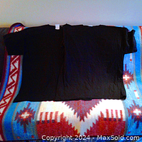 Two men's black t-shirts side by side laid flat on a patterned blanket, showing front and back sides