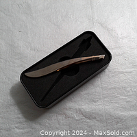 Curved eyebrow tweezer with gold tone dipped tipped angled ends in black foam case.