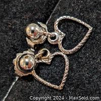 Close-up photo of the sterling silver heart-shaped dangle earrings showing the detailed braided texture and smooth stud backing on black fabric.