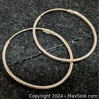Pair of round sterling silver hoop earrings against black background, highlighting smooth polished finish and hinged clasp.