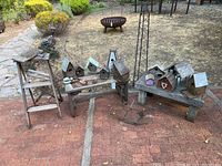 Wide view of assembled birdhouses and decorative items on wooden benches and stand outdoors