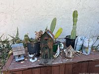 View showing arrangement of three wooden birdhouses, some potted cactus plants in black speckled pots, and several small decorative items on a wooden table against a stucco wall.