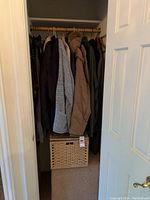 Photo showing multiple coats and jackets hanging on a wooden rod with a woven basket below in the entryway closet.
