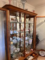Full cabinet view showing top display of colored glass vases and shelves of assorted crystal and porcelain
