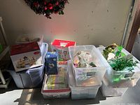 View of several plastic bins containing various holiday decorations, boxes with Christmas related images.