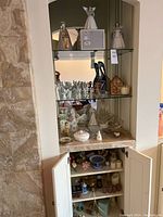 Wide view of glass shelves with porcelain and ceramic figurines including angels, religious figures, glassware and decorative wooden item.