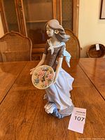 Front view of the Lladro porcelain figurine showing the woman holding a floral plate with multiple pastel flowers and a small blue base resembling waves.