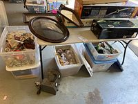 Image showing multiple bins with fall-themed glass decor items wrapped in newspaper, three oval framed wall art pieces on table, and vintage electrical device on floor.