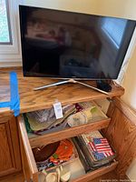 Front view of Samsung 32-inch TV on wooden furniture with drawers open showing kitchenware and decorative items