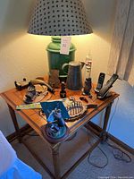 Side table with lamp on top and assorted miner collectibles scattered on table surface including figurines, metal containers, pocket watch, small lantern, cordless phones.