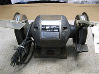 Front view of the 6" double ended bench grinder showing metal casing, power cord, and label with specifications.