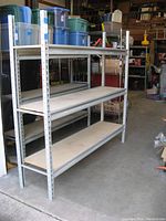 Front and side view of the assembled shelving unit showing the steel frame and wooden shelves in a workshop environment.
