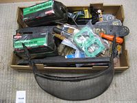 Photo of chainsaw accessories in a cardboard tray including multiple bottles of 2 cycle engine oil, sharpening files and guides, protective mesh face shield, and several chainsaw bars under accessories.