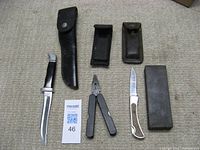 Full set of knives, multi-tool, sharpening stone, and leather sheaths laid out on carpeted floor