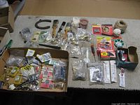 Overview photo of lot showing all items spread out including window locks, paint brushes, hardware pieces, horseshoe, string, screwdrivers, and packaging.