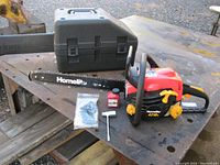 Homelite model 4218C 18-inch chainsaw with an attached bar and chain, bottle of two stroke oil, new sealed Carlton chain, and a maintenance tool displayed on a metal surface.