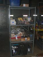 A metal shelving unit with four shelves, loaded with various boxes and items for scale. Light rust is visible on shelving surfaces. The shelving unit stands tall in a garage or storage area.