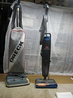 Oreck XL Xtended Life upright vacuum on the left with cloth bag and Bissell Steam & Sweep upright vacuum/steam cleaner on the right, both standing upright on carpet.