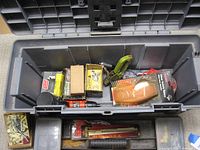 Open gray plastic toolbox showing various hand tools, boxes of staples, staplers, small torch, and a paint brush inside.