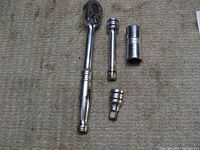 Top view of Snap-On ratchet, two extensions and double ended socket on carpeted floor.