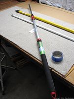 Three painters' poles displayed on a table, showing padded handle, yellow fiberglass pole, and white pole.
