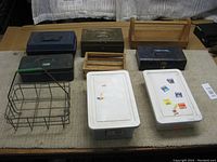 Overview photo of the vintage wire milk bottle carrier, three metal closed boxes, one plastic closed box, open wooden toolbox, two plastic Rubbermaid storage boxes with lids, and small wooden decorative crate all arranged on a carpeted surface.