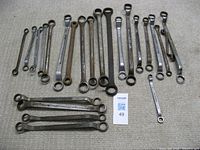 24 double box end wrenches laid out on a carpeted floor, showing various sizes and wear marks, metal with visible rust and usage wear.